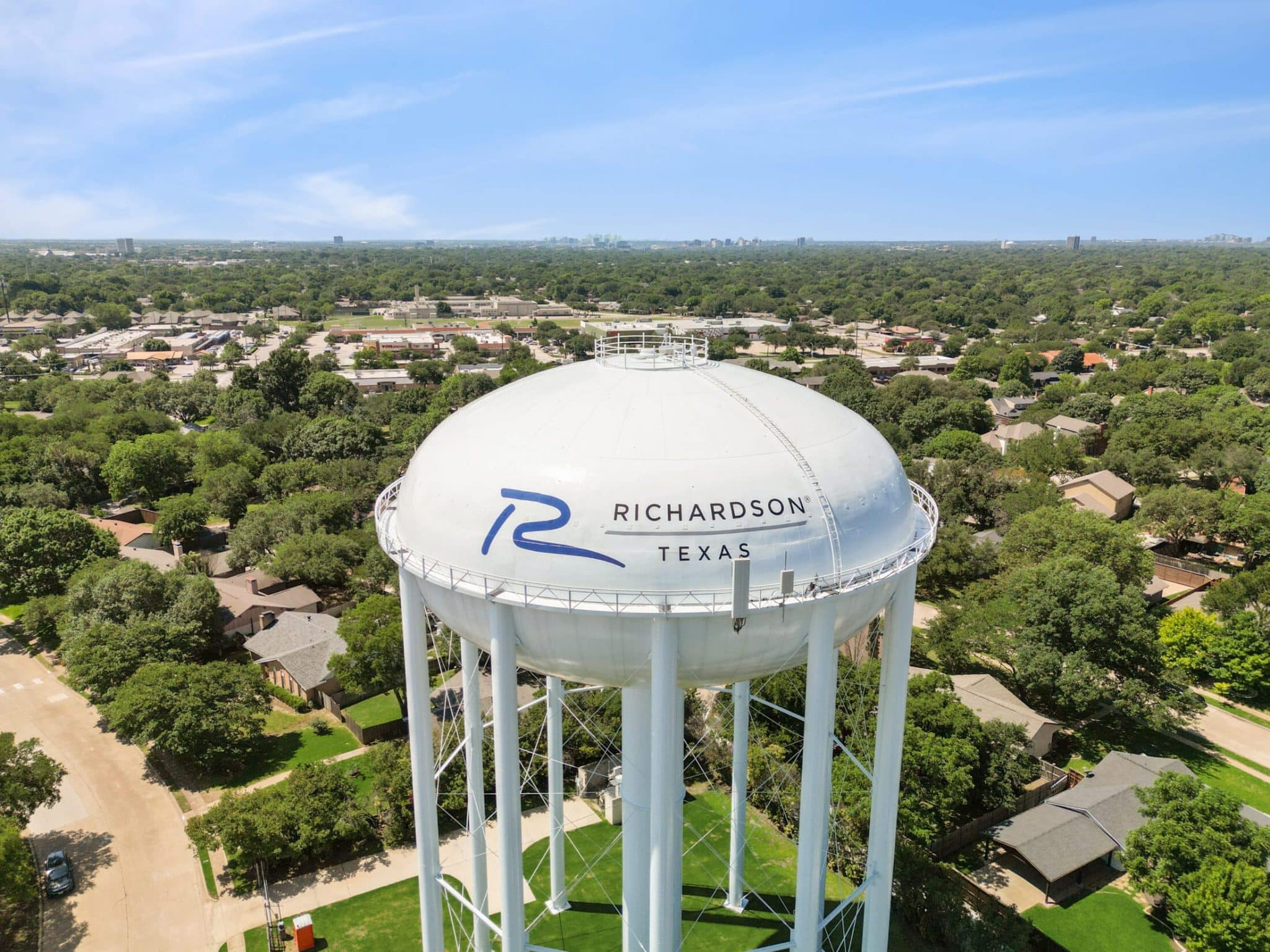 Richardson Texas water tower with logo, surrounded by residential area and greenery, symbolizing local community for cash for junk cars service.